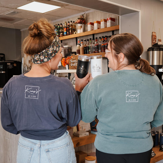 Two women in a kitchen or bar setting, one holding a black cup.